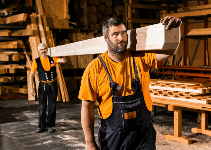 Zwei Mitarbeiter tragen eine Holzplanke auf ihren Schultern