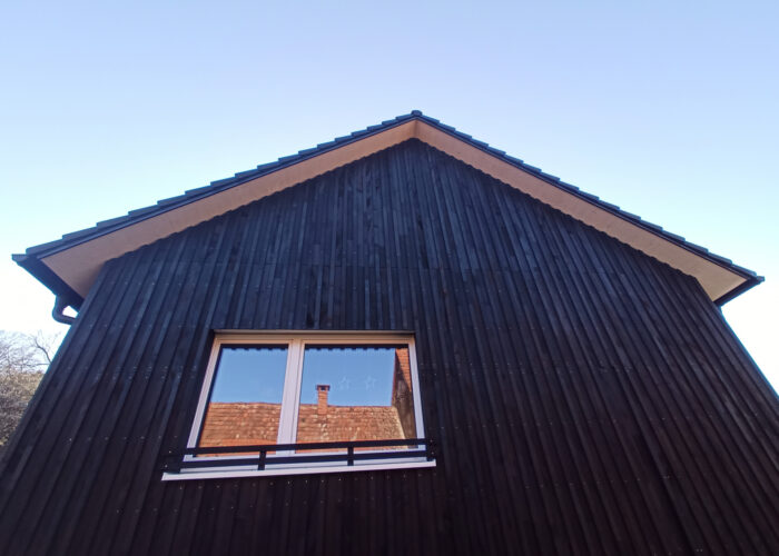 Vorderseite eines schwarzen Holzhauses mit einem Fenster